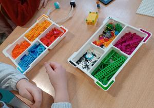 Dzieci siedząc przy stoliku słuchają instrukcji dotyczących programowania Lego Education.