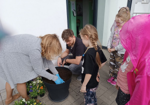 Nauczycielka pokazuje uczniom jak należy przygotować ziemię przed sadzeniem kwiatków.