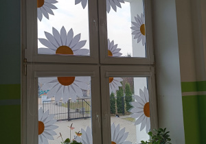 Wiosenna dekoracja z papieru, biało-żółte kwiaty, umieszczona na oknie.