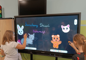 Uczennice wykonują rysunki zwierząt na tablicy multimedialnej.