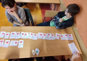 Uczniowie siedzą przy stoliku, na którym rozłożone są karty "Walentynkowego treningu emocji".