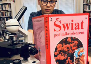 Chłopiec przeglądający książkę w czasie pracy z mikroskopem.