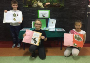 3 uczniów prezentuje zielniki umieszczone na szkolnej wystawie.