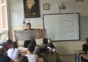 Wykład poświęcony historii zwyczajów i obyczajów Białorusinów a w tle nauczyciel pokazuje ręcznik białoruski w Szkole Podstawowej nr 26 w Białymstoku